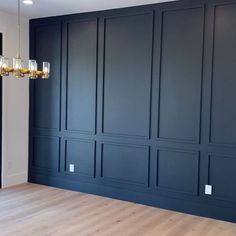 an empty room with dark blue walls and wood flooring in the center is a chandelier