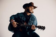 a man wearing a cowboy hat and playing an acoustic guitar