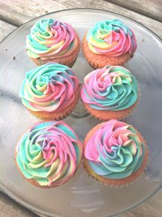 six cupcakes with colorful frosting on a glass plate