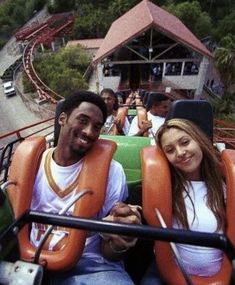 two people sitting on a roller coaster at an amusement park, smiling for the camera