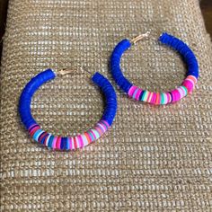 two pairs of blue and pink hoop earrings sitting on top of a piece of fabric