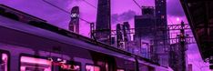 a train traveling down tracks next to tall buildings in the city at night with purple hues