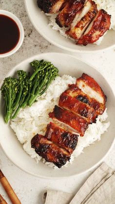 two plates with meat, rice and broccoli next to chopsticks on a table