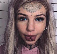 a woman with tattoos and piercings on her face is making a funny face for the camera