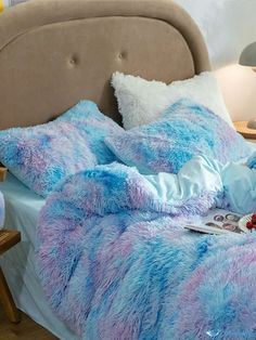 a bed covered in blue and pink fluffy blankets next to a night stand with a lamp on it