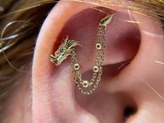 🐉✨ Embrace the power of the dragon with our custom "1976" piece from Juniperr jewelry, a 14k gold dragon connected with a chain.    🌟✨ This stunning upgrade to an existing piercing symbolizes strength, wisdom, and good fortune.  Our talented piercer Celia helped customize to this client her idea and create something truly special that fits her anatomy.  Make an appointment with our professional piercers to create your self your new unique piercing statement!! Fantasy Ear Piercings, Dragon Industrial Piercing, Celestial Ear Piercings, Dragon Earring Cuff, Gold Dragon Earrings, Gold Dragon, Traditional Earrings