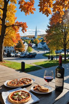 two pizzas and a glass of wine on a picnic table with autumn foliage in the background