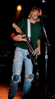 a man standing in front of a microphone while holding a guitar