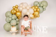 a baby sitting on a chair in front of balloons and cake with the word one spelled out