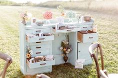 an old desk with drawers and flowers on top is sitting in the middle of a grassy field