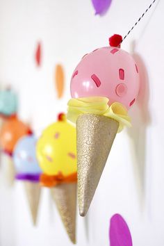 an ice cream cone hanging from a string with confetti and balloons in the background