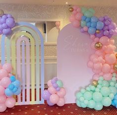 there is a balloon arch with balloons all over it and a sign on the wall