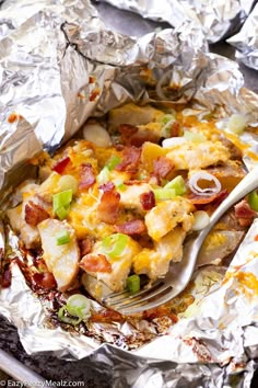 a fork in a foil covered dish with potatoes and bacon