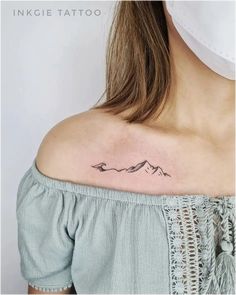 a woman's shoulder with a small tattoo on her left shoulder and mountains in the background