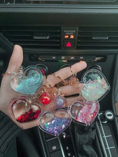 the person is holding their heart shaped keychains in front of her car's dashboard