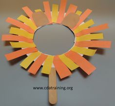 an orange and yellow paper sunflower on a gray surface with a wooden stick sticking out of it