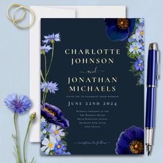 a wedding card with blue flowers on it next to a pen and flower bouquets