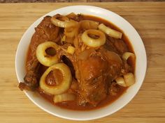 a white bowl filled with meat and onions on top of a wooden cutting board next to a knife