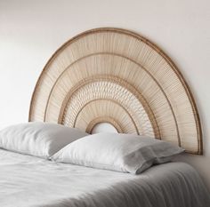 a bed with white sheets and pillows in a room next to a wall mounted wicker headboard