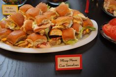 a pile of sandwiches sitting on top of a white plate next to tomatoes and lettuce