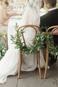 a bride and groom sitting at a table with greenery