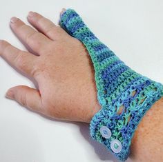 a hand with a blue and green crocheted wrist warmer on it's arm