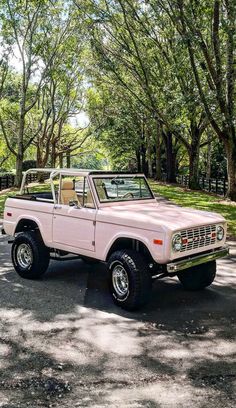 a pink pick up truck parked on the side of a road next to some trees