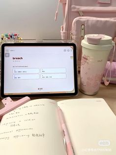 an open laptop computer sitting on top of a wooden desk next to a pink cup