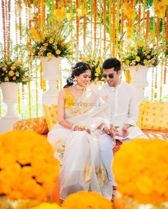 a man and woman sitting next to each other in front of yellow flowers on the ground