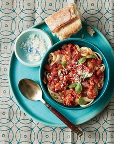 a blue plate topped with pasta and meat next to bread on top of a table