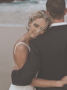 a man and woman standing next to each other on the beach in front of the ocean