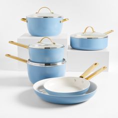 blue pots and pans with gold handles are stacked on top of each other in front of white boxes