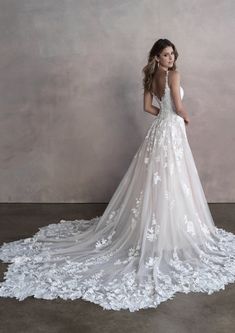 a woman in a white wedding dress with flowers on the skirt, standing against a wall