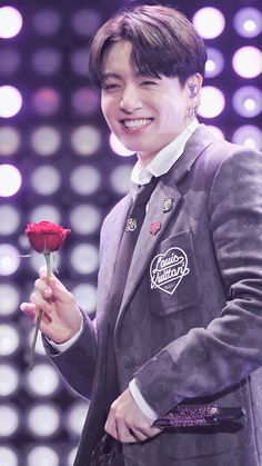 a man in a suit holding a rose and smiling at the camera while standing on stage