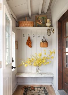 a white bench with yellow flowers and baskets on the wall in front of an open door