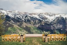 an outdoor ceremony set up with wooden chairs and floral arrangements in front of snow - capped mountains