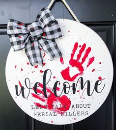 a welcome sign hanging on a door with red handprints and a gingham bow