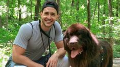 a man kneeling down next to a dog in the woods with his tongue hanging out