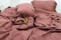 an unmade bed with two pillows and a glass on the bottom half, in front of it