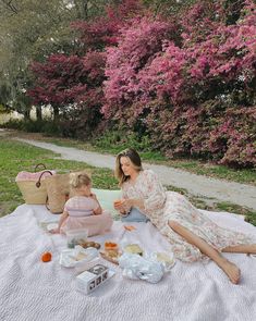 a woman and child sitting on a blanket in front of some trees with pink flowers