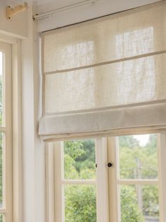 two windows with roman blinds in front of them and trees out the window behind them