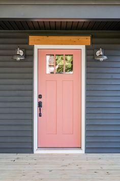 a pink front door on a gray house with wood flooring and two lights above it