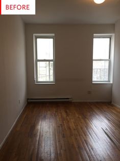 an empty room with two windows and hard wood flooring in the middle of it