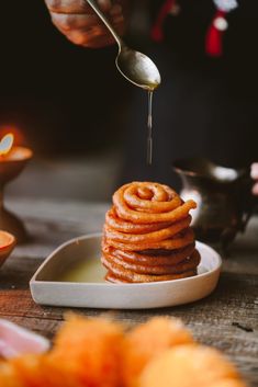 a person is pouring syrup on top of some cinnamon buns in a white dish