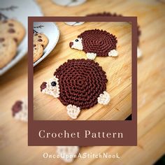 two crocheted sheep coasters sitting on top of a wooden table next to cookies