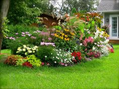 a flower garden in front of a house with lots of colorful flowers and greenery