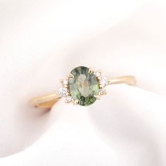 a ring with an oval cut green stone surrounded by three small white diamonds on top