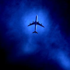 an airplane is flying in the sky with clouds around it and blue light coming from below