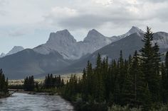 a river running through a lush green forest covered hillside next to tall mountain range in the distance