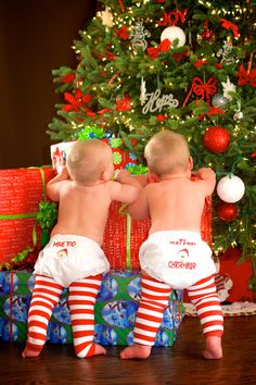 two babies in diapers are sitting next to a christmas tree with presents on it